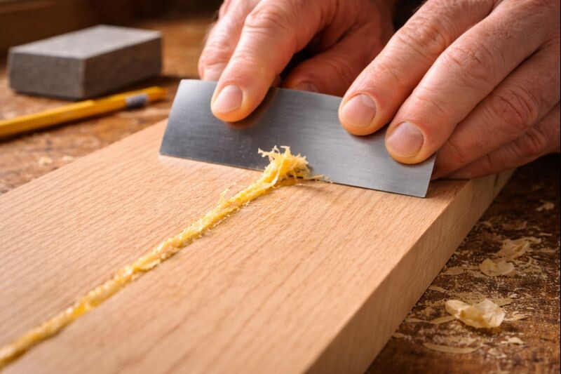 using a card scraper to shave dried glue from bare wood