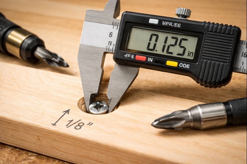 Macro view of a countersunk screw set 1/8 inch deep in maple, caliper showing depth before filling and sanding.