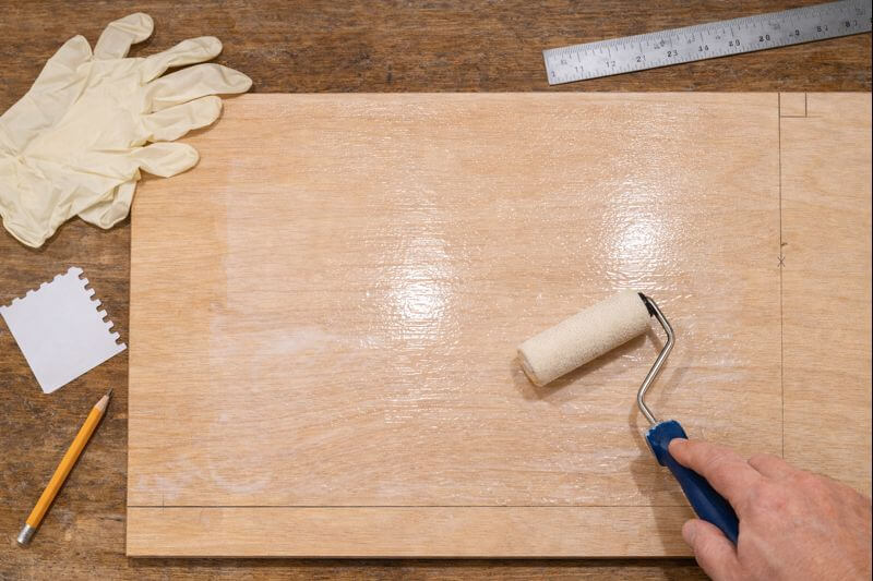 roller spreading thin glue layer on plywood sheet