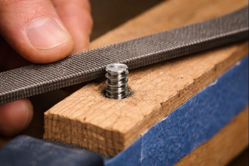 hand file smoothing a cut screw end so it won’t snag skin or scratch a countertop