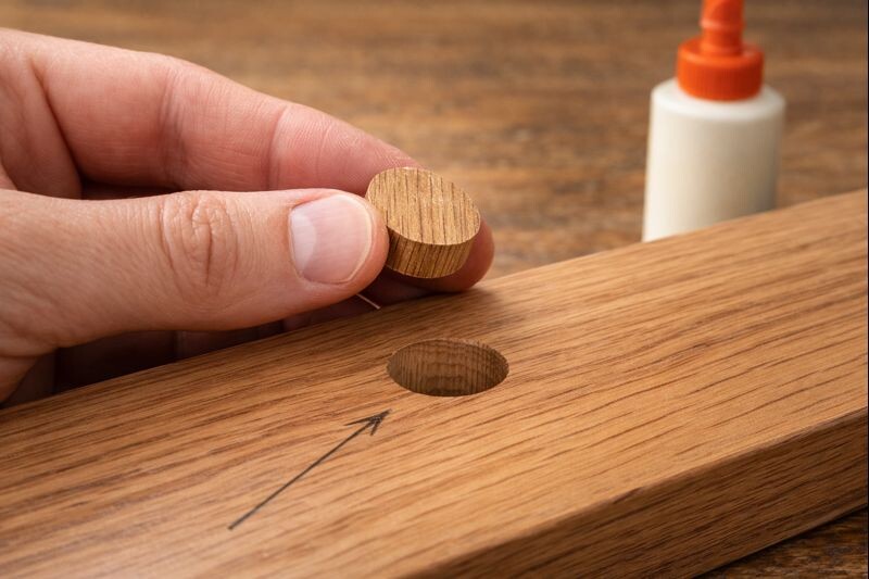 Hands rotating a wood plug to match the board’s grain direction before gluing, showing why alignment hides the repair.