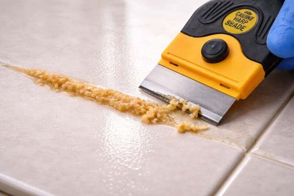 plastic razor scraper lifting cured glue from glossy tile