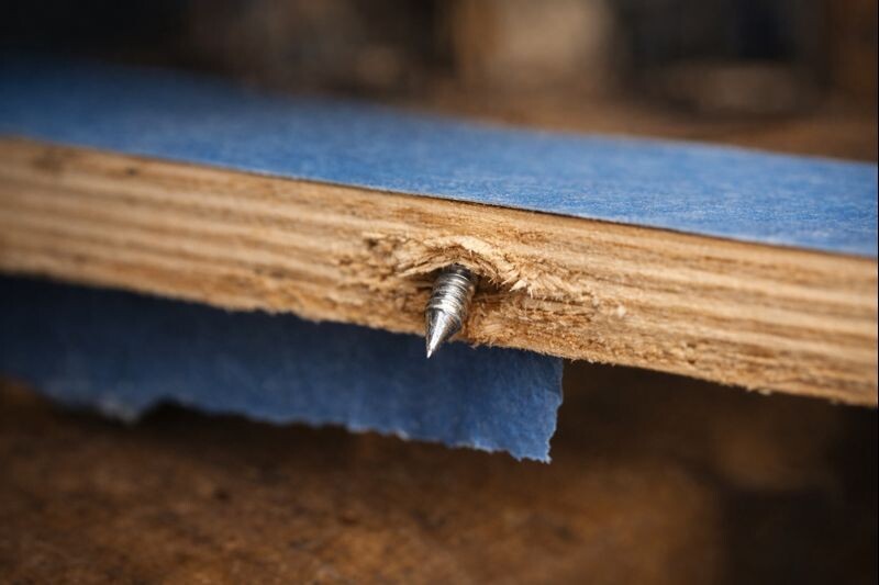 close view of a screw point poking through plywood underside with painter tape protecting the surface