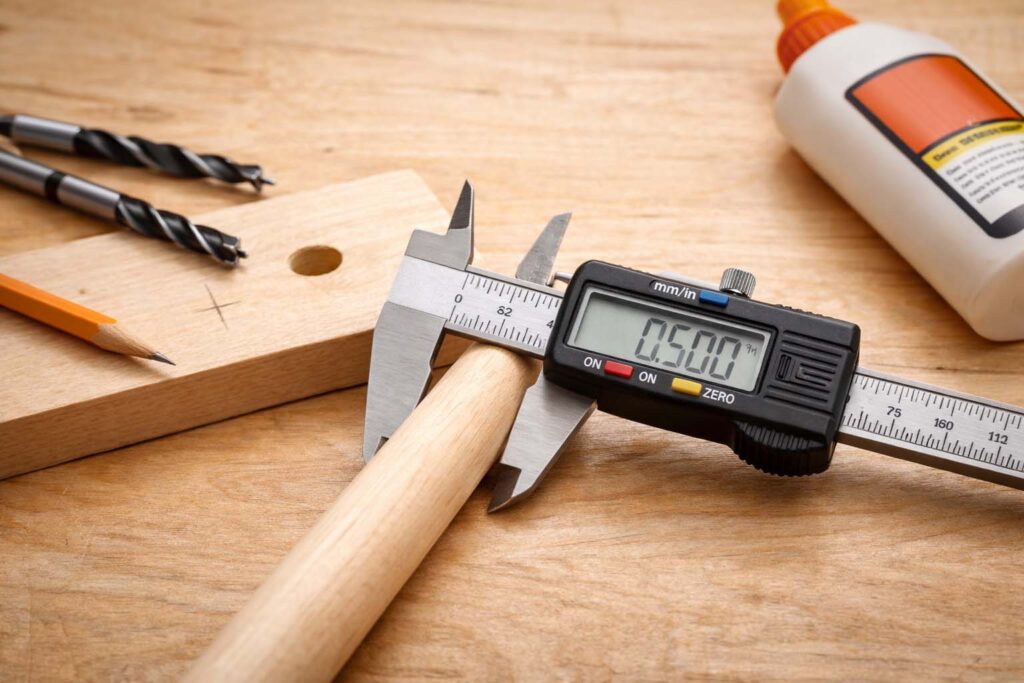 digital calipers measuring a maple dowel next to a drilled test hole